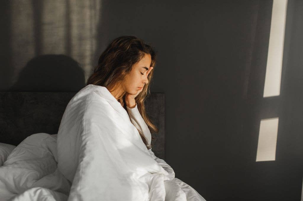 Woman yawning and can't wake up in morning. Sitting in bed covered with blanket.