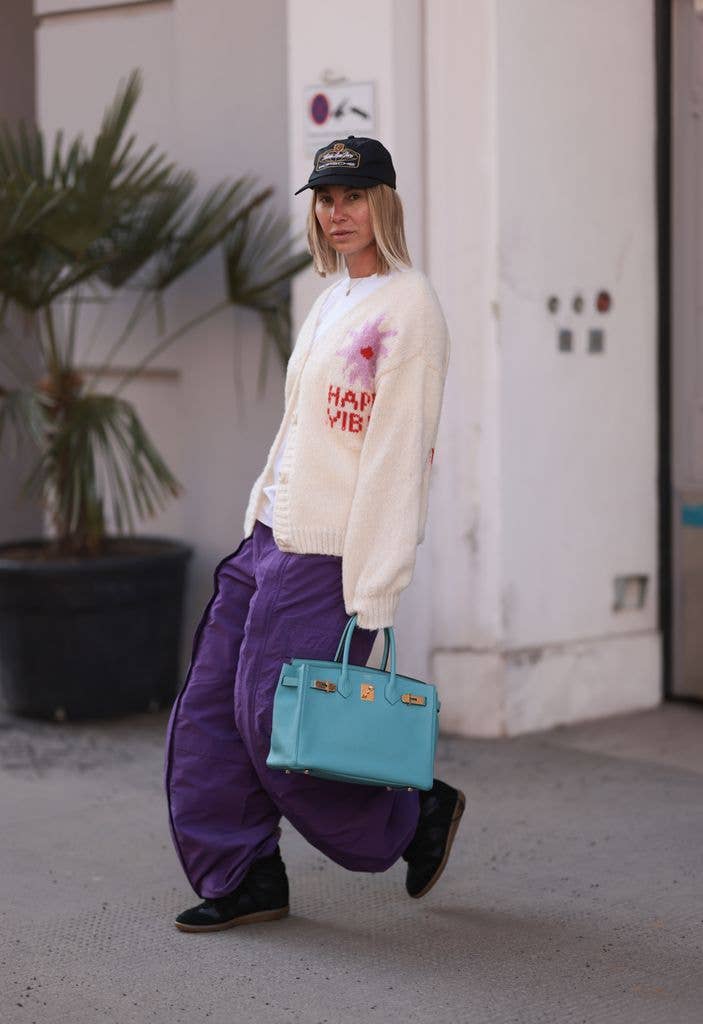 Karin Teigl seen wearing Aime Leon Dore x Porsche black logo cap, Viktoria Louise white cotton basic shirt, Ukiyo cream white oversized knit cardigan, Gucci purple oversized cargo pants, HermÃ¨s baby blue leather Birkin bag and Isabel Marant black wedge sneaker high top Bekett shoes, on February 19, 2025 in Vienna, Austria. (Photo by Jeremy Moeller/Getty Images)