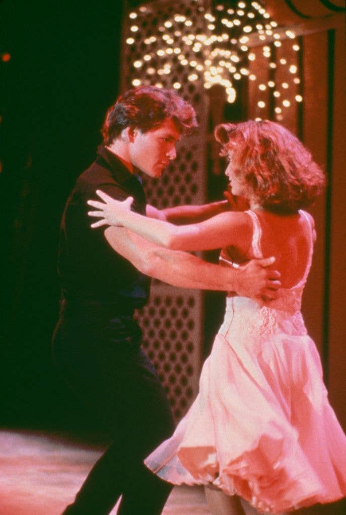 Patrick Swayze and Jennifer Grey stare at one another mid dance with their arms structured and hands held on one another's shoulder and back. 