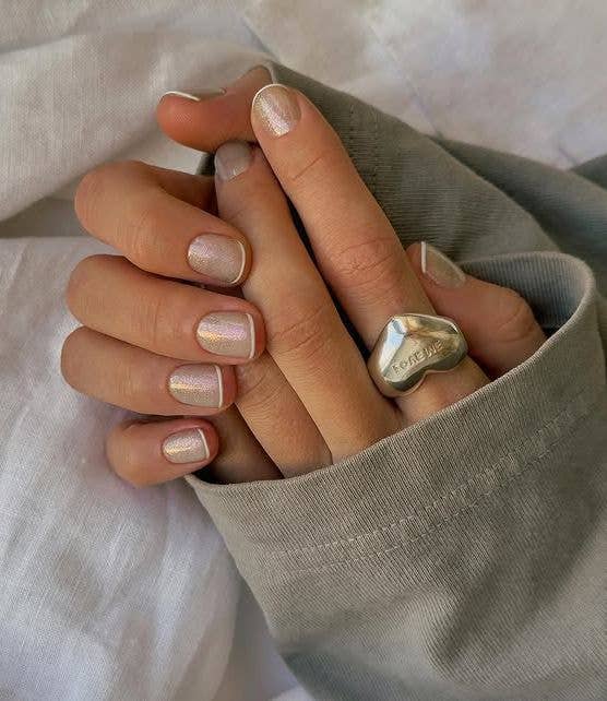 A modern glitter French manicure on short nails with an iridescent base and a crisp, white micro-line tip.