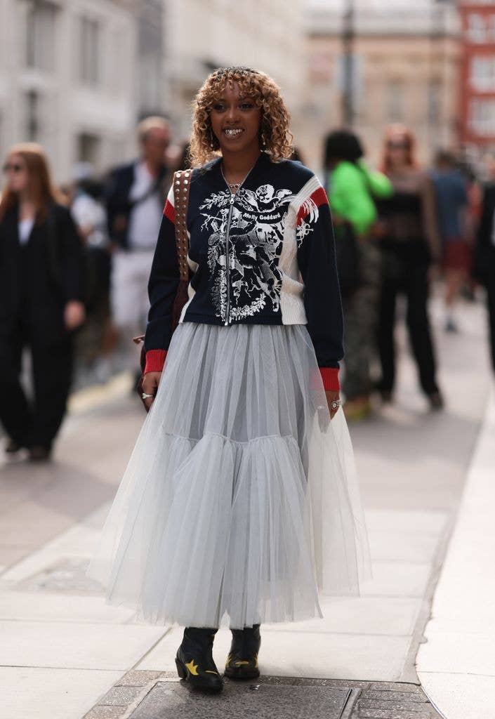 Nia Archives seen outside Molly Goddard show wearing white and red embroided Molly Goddard jacket, a white tulle long skirt, silver rings and black and yellow leather cowboy boots gelduring London Fashion Week September 2023