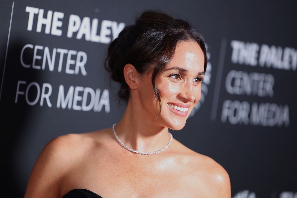 Meghan Markle smiling in a shoulderless dress