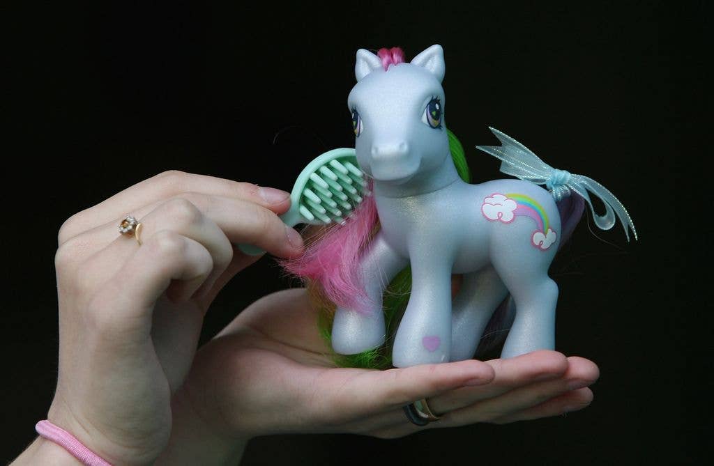 A fan holds a My Little Pony on her upturned palm, using the other hand to brush its mane.