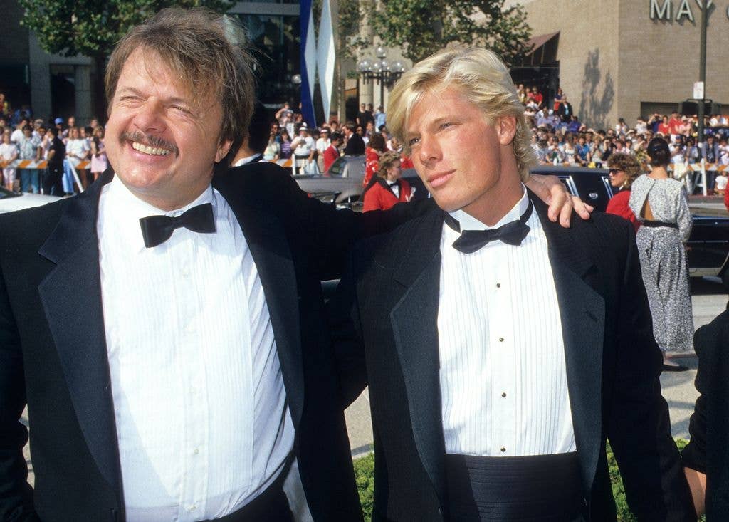 John Karlen and son Adam wear matching tuxedos and hold one arm around each other.