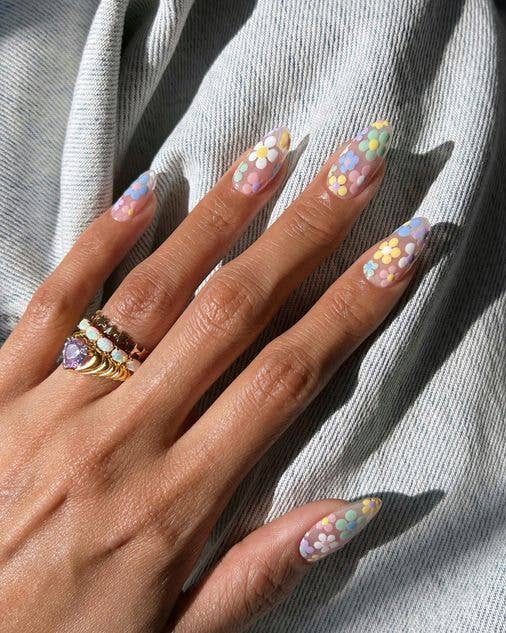 Hand-painted floral manicure with tiny white and yellow daisies over a sheer pastel lilac base