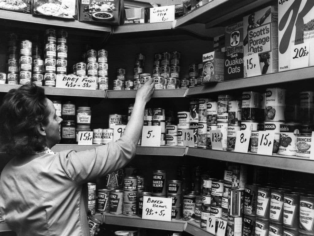 The owner of a small grocers shop in London arranges and prices a stock of tinned foods. 