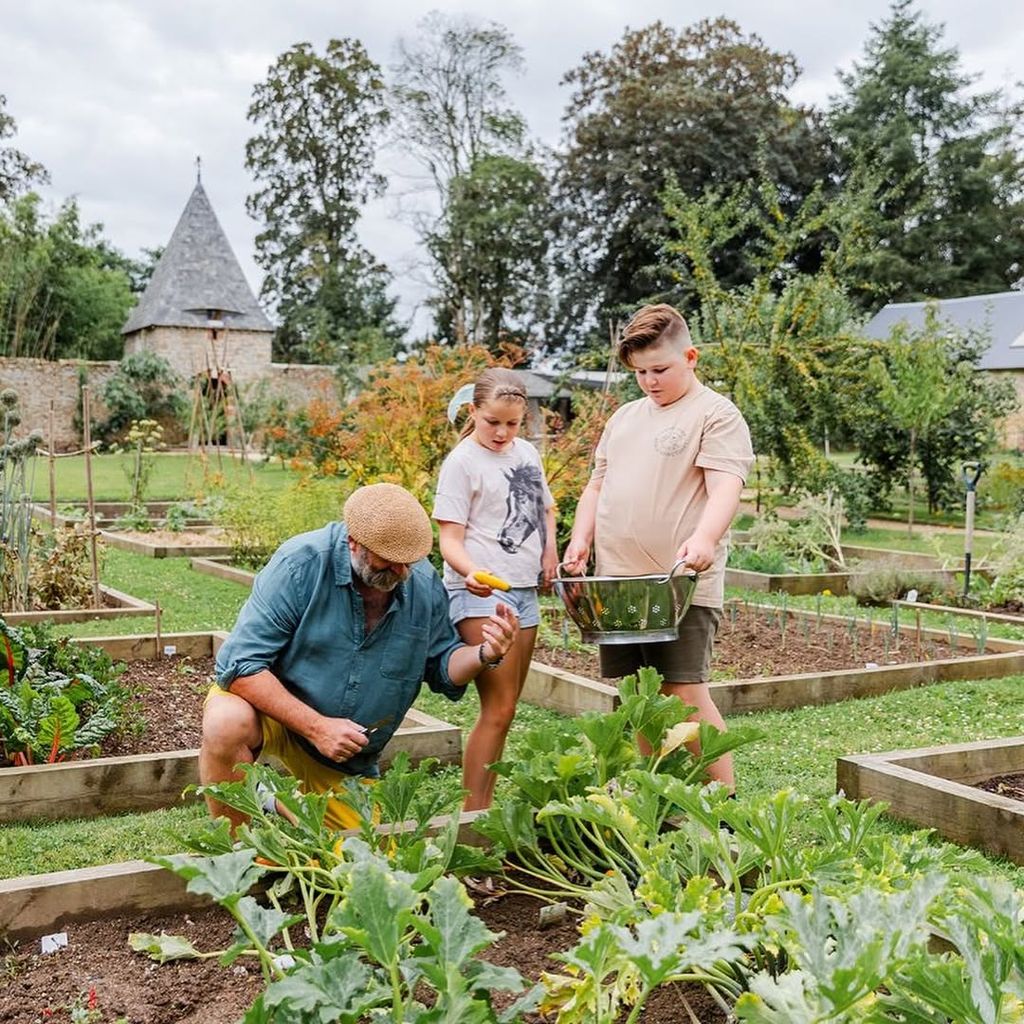 Dick Strawbridge kneeling down to collect vegetables in garden while Arthur and Dorothy look on 