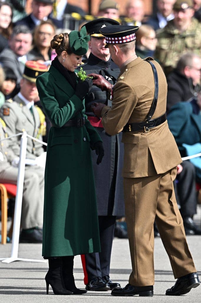 Catherine, Princess of Wales laughs while being presented with traditional sprigs of shamrock by officer