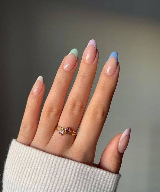 Reimagined French manicure with multi-colored pastel tips in peach, lilac, and mint green on a nude base