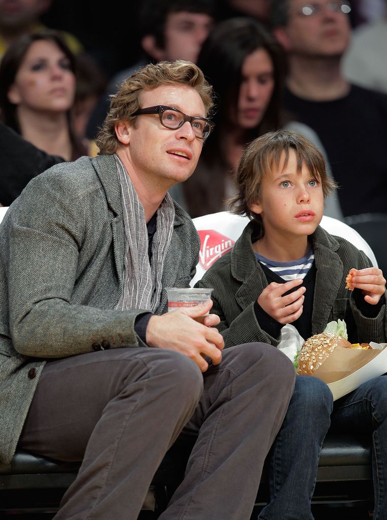 Claude Blueu Baker holds snacks in mid air next to father Simon Baker at a game in the Stapes Center.