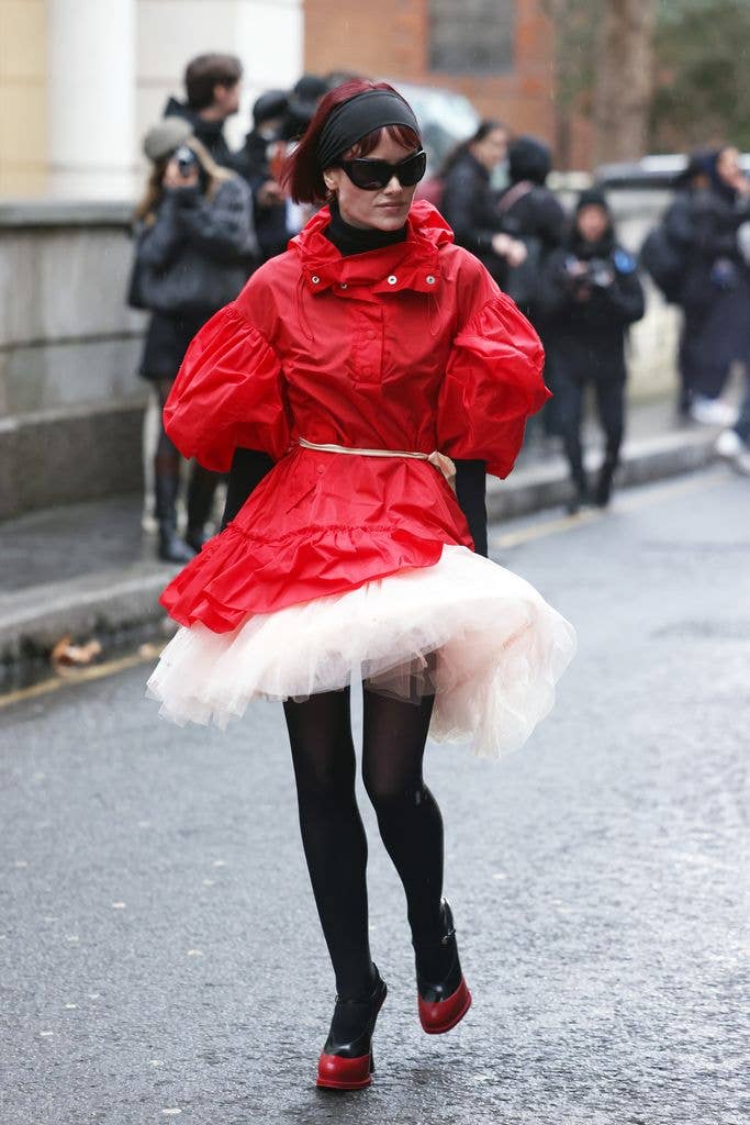 Guest wearing red puffer coat, pink tutu and red heels with sunglasses outside Simone Rocha February 2025 Show at Goldsmith's Hall during London Fashion Week F