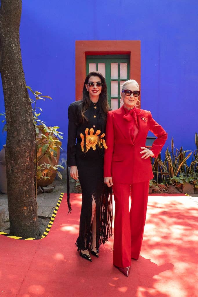 Anne Hathaway in black dress and Meryl Streep in red suit pose for a photo during a conference for The Devil Wears Prada 2