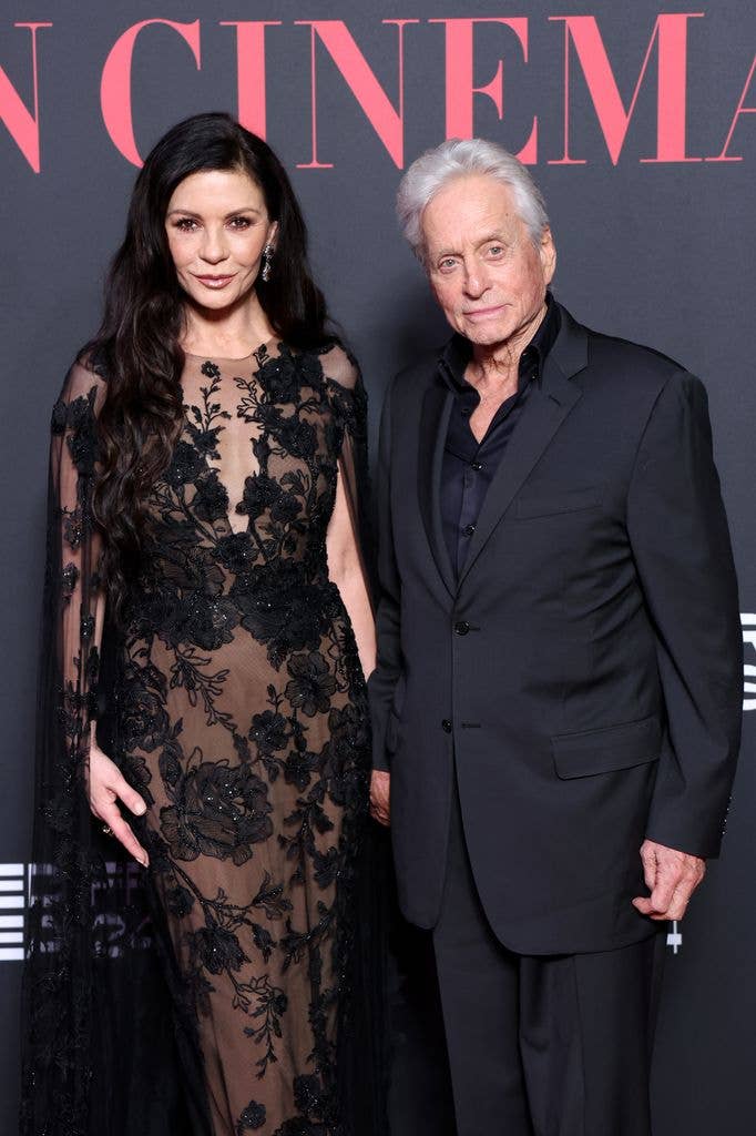 Catherine Zeta-Jones wears a black lace dress with a nude slip and stands next to Michael Douglas who wears a black suit.