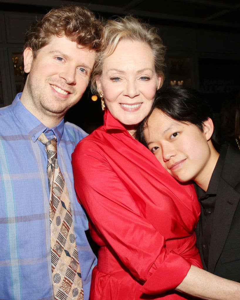 Connor Gilliland in a blue check shirt with beige tie rests his head against mother Jean's forehead. Jean wears a red shirt dress rolled up at the elbow. She holds son Forrest who wears a black shirt and rests his head on his mother's chest.