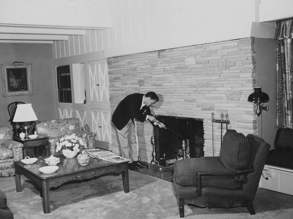 Frank Sinatra stokes a fireplace in his living room.