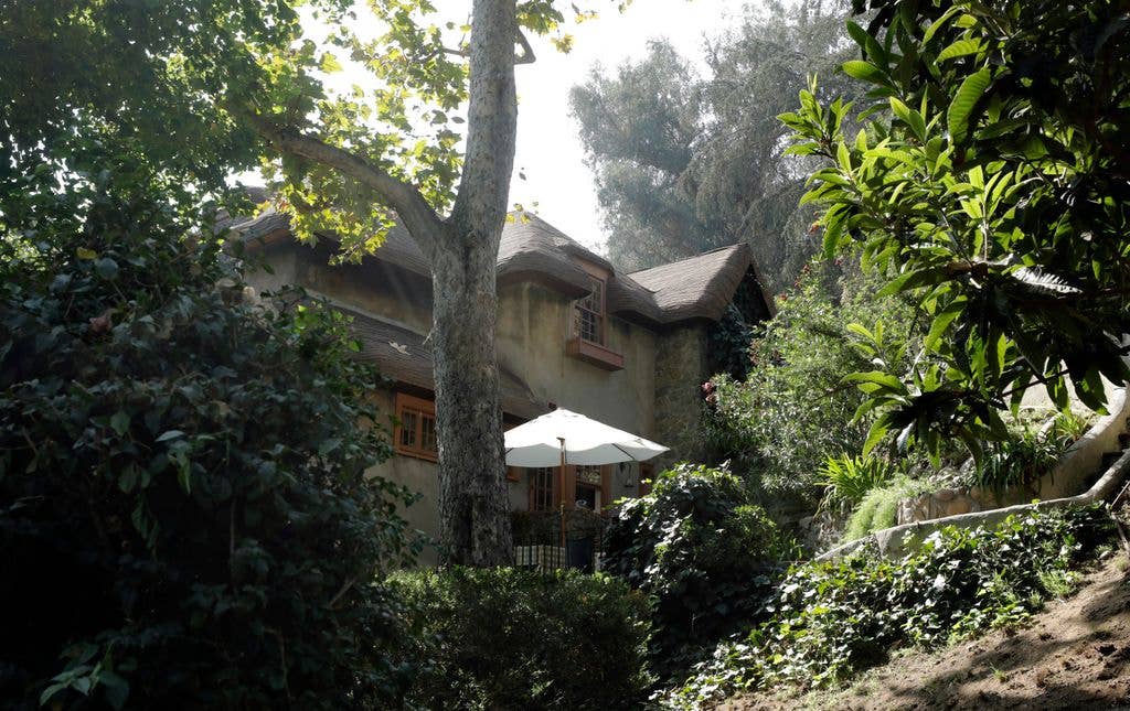 Humphrey Bogart's home styled as an English Cottage and pictured from the road, partly hidden behind trees.