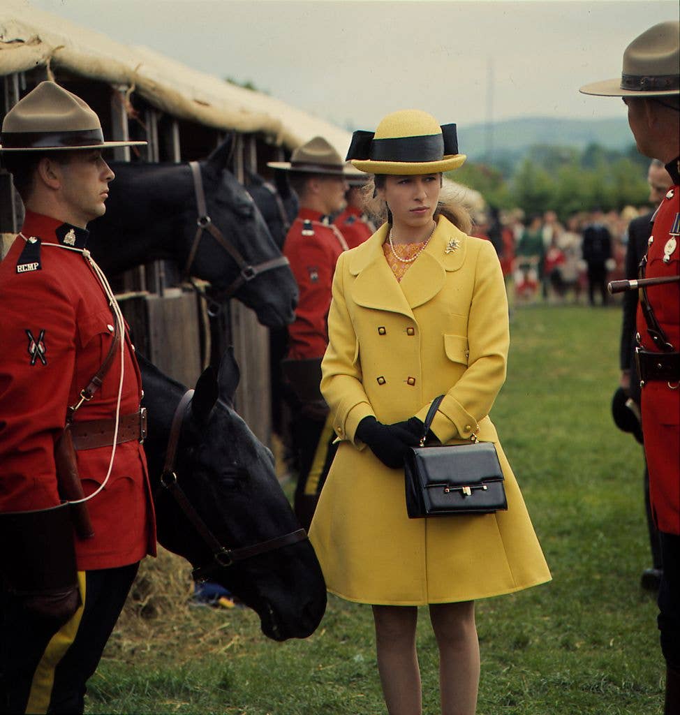 Princess Anne in canary yellow coat and hat at the Bath and West Agricultural Show beside police officers and horses