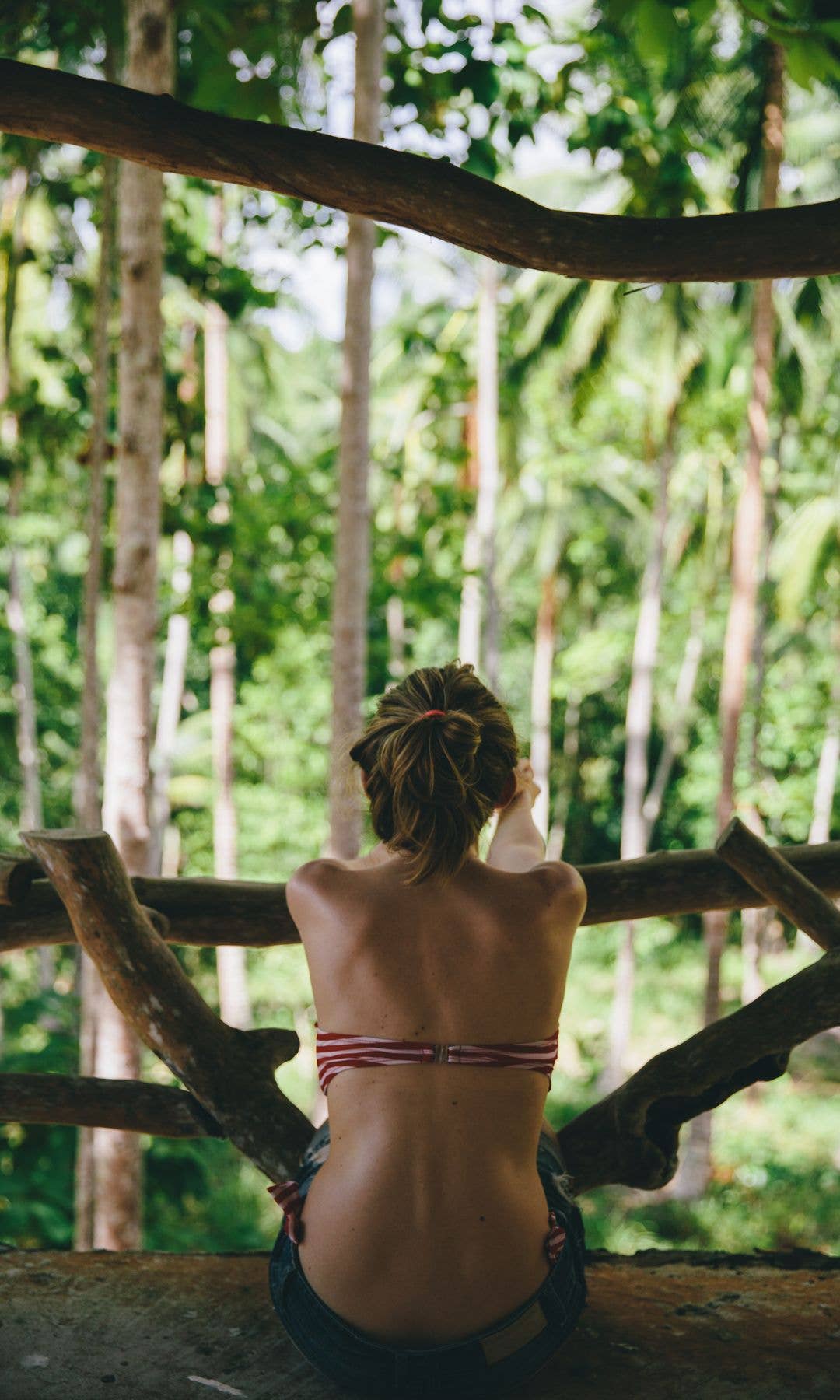 Woman sitting in a treehouse in the jungle with her back to the camera