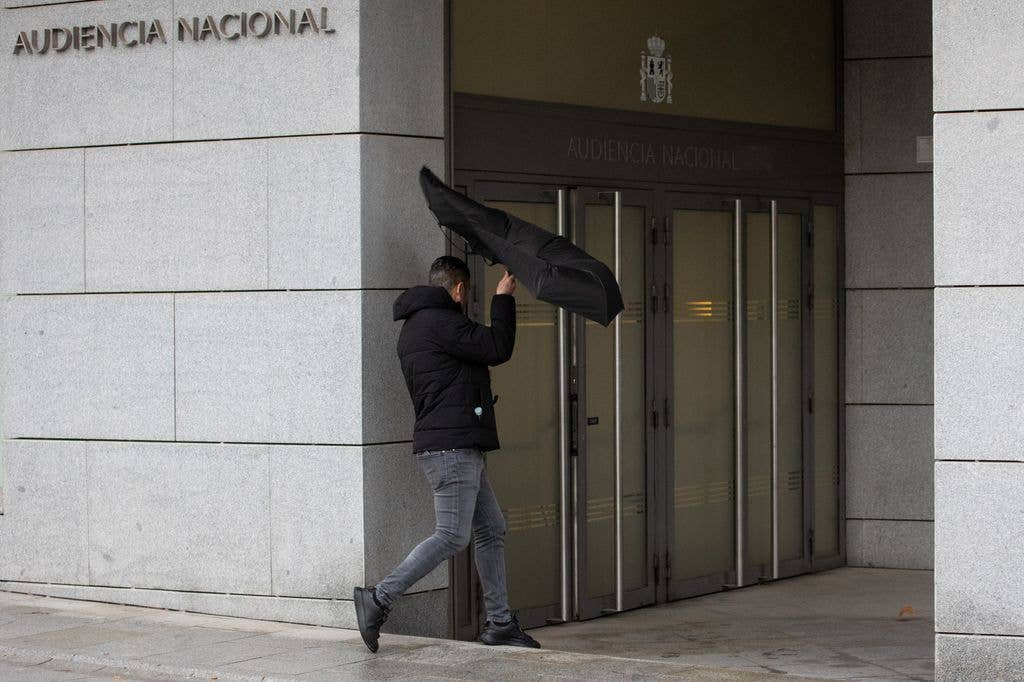 Backshot of Manuel Blanco Vega arriving at court with an inside out umbrella
