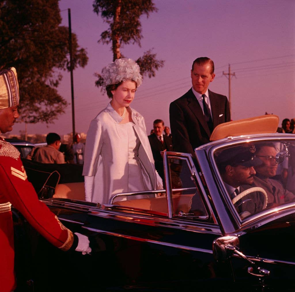 Queen Elizabeth II and Prince Philip stand in an open-top car while travelling through Delhi on a state visit to India, 1961