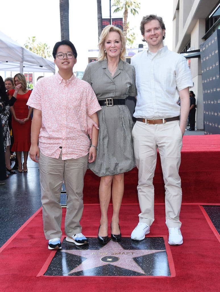 Jean Smart in a belted black and white pattern dress, holding arm around son Connor who wears a white shirt and brown belt with light trousers.