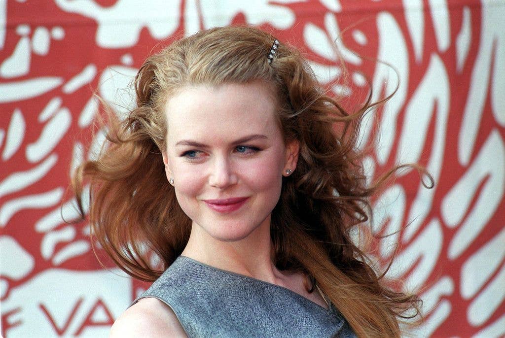 Nicole Kidman looks back over her right shoulder in a grey textured dress and her red hair blowing in a strong breeze.