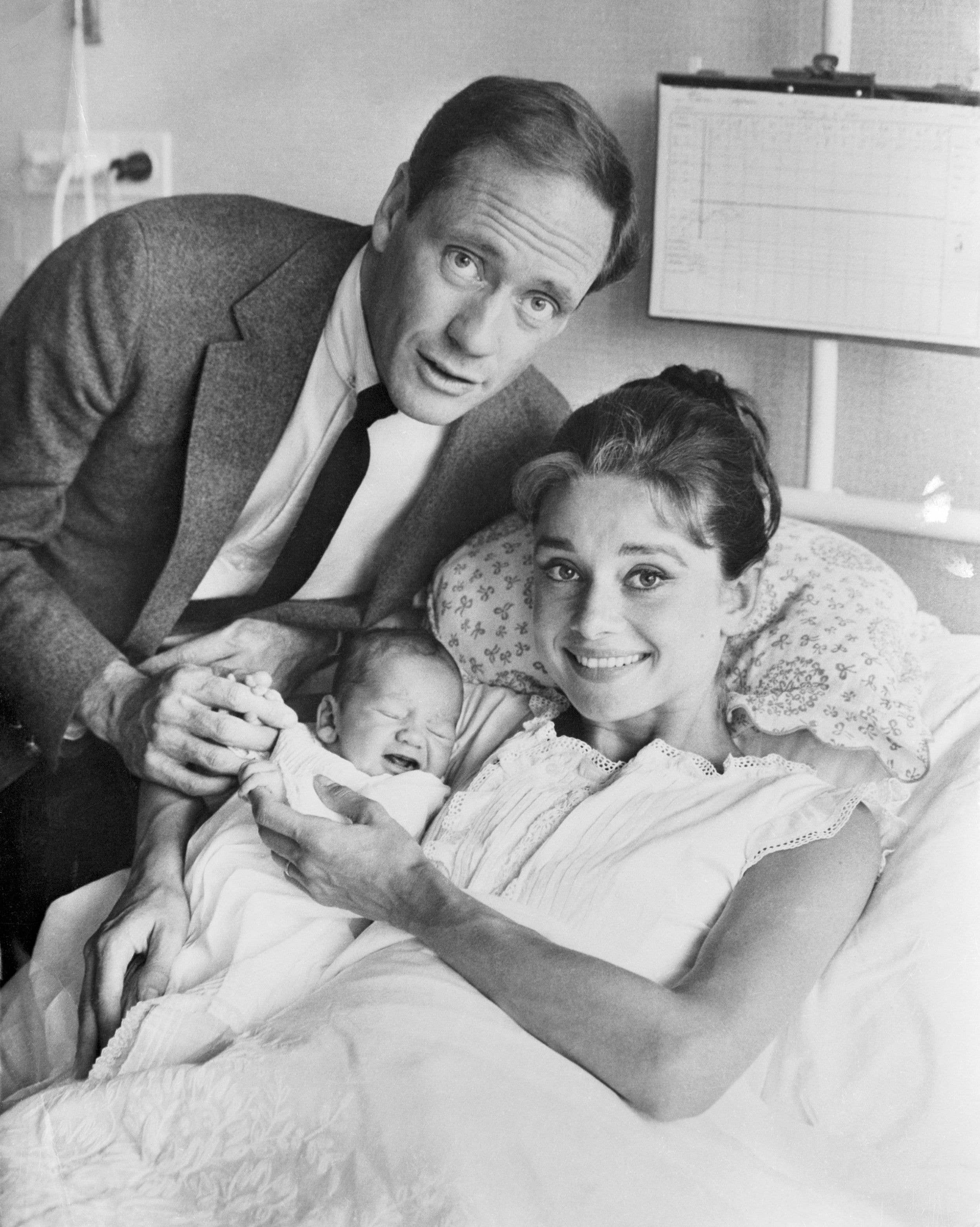 Audrey Hepburn holding her baby Sean in the hospital bed with husband, Mel Ferrer beside her