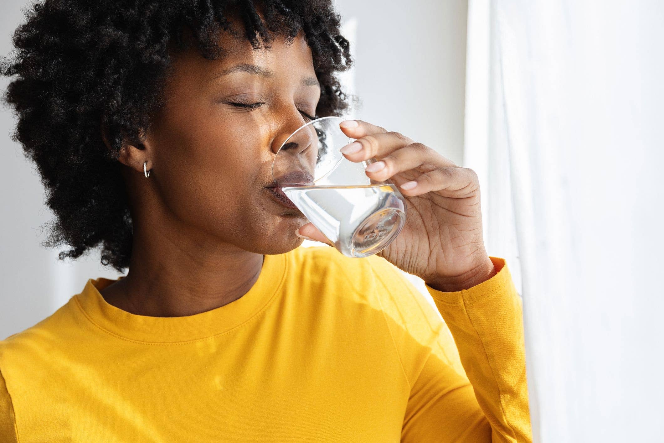 Young black woman drinking a glass of fresh water, promoting a healthy lifestyle and proper hydration