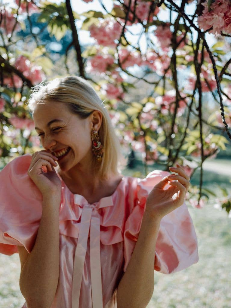 A woman in a pink dress laughing amongst the pink blossom