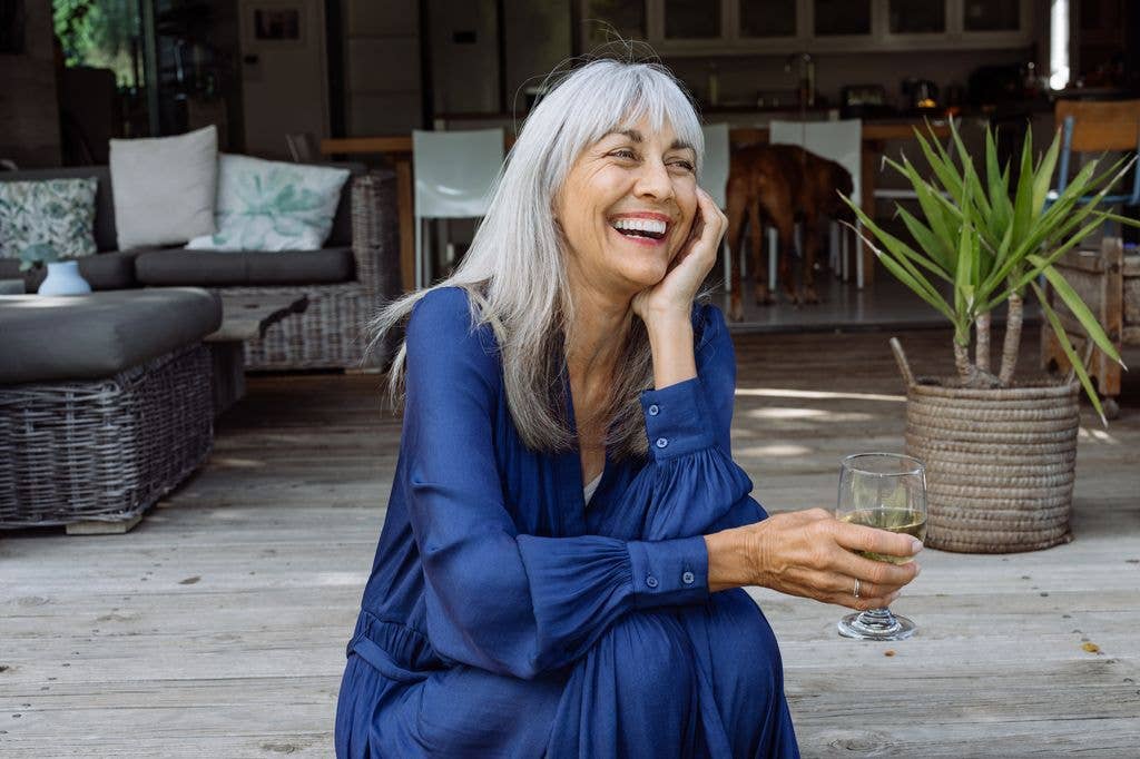 A sophisticated woman enjoys a peaceful afternoon on her patio, exuding joy and contentment with a glass of wine.