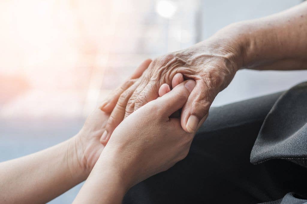 Two hands, one elderly and one younger, holding each other in a comforting gesture.