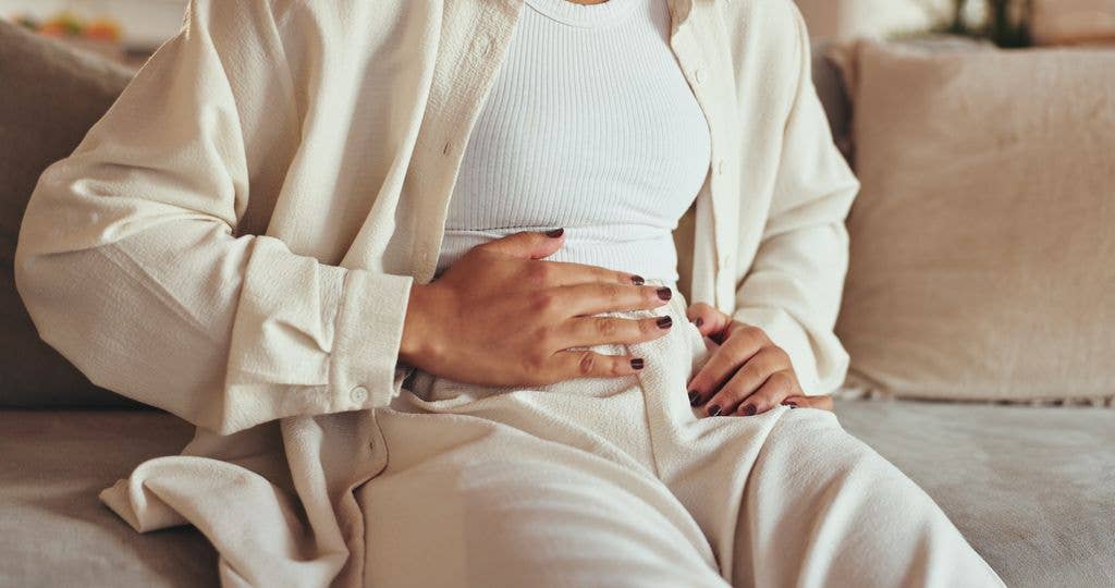 Woman, hands and stomach pain of menstruation on sofa with period cramps, bloating or pms in home