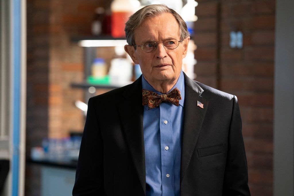 David McCallum as Medical Examiner Dr Donald "Ducky" Mallard in a dark suit jacket, American flag pin, blue shirt and paisley patterned red tie.