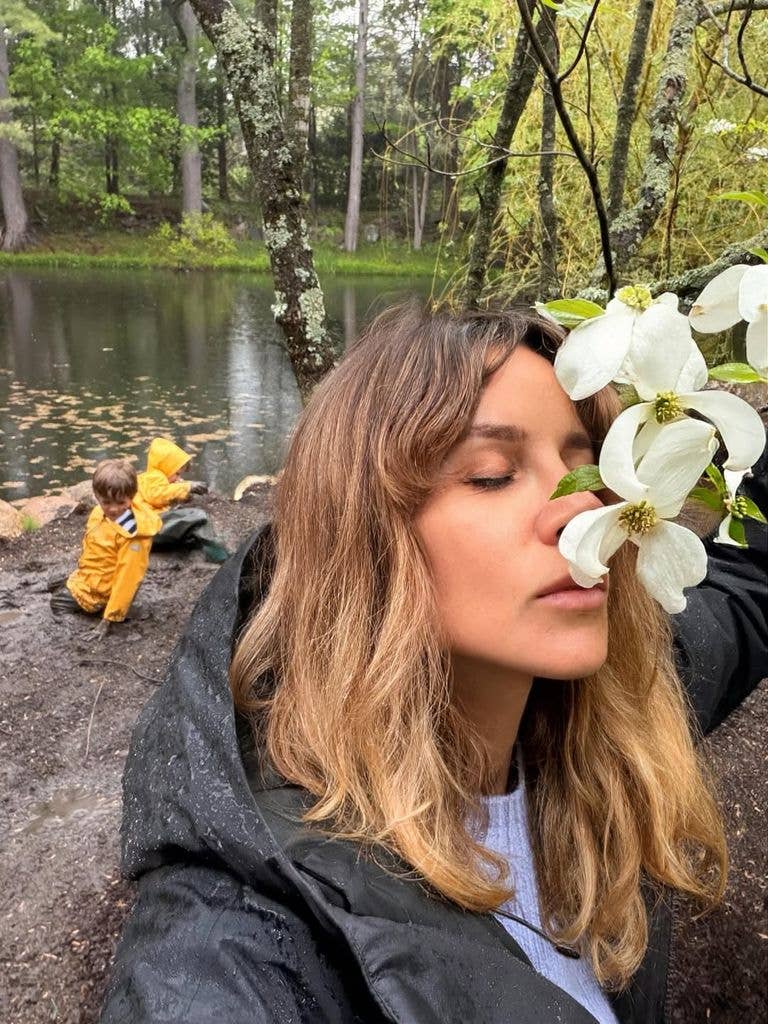 Alejandra Gere sniffs flowers while her sons play by the water behind her, shared on Instagram