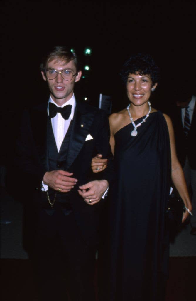 Richard Thomas wears a tux and walks with his wife Alma Gonzales who holds a hand on his arm and wears a dark one shoulder dress.