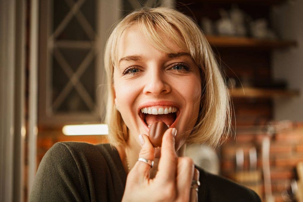 woman eating chocolate treat in kitchen while looking ahead