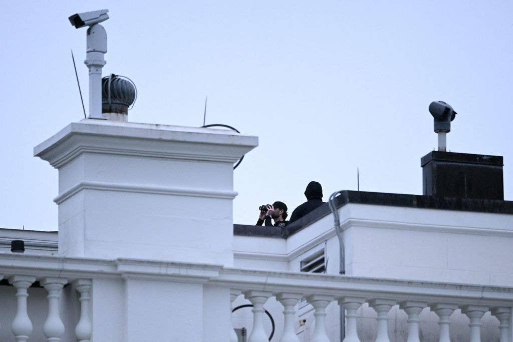 A police officer uses binoculars on the roof of a building at the White House 