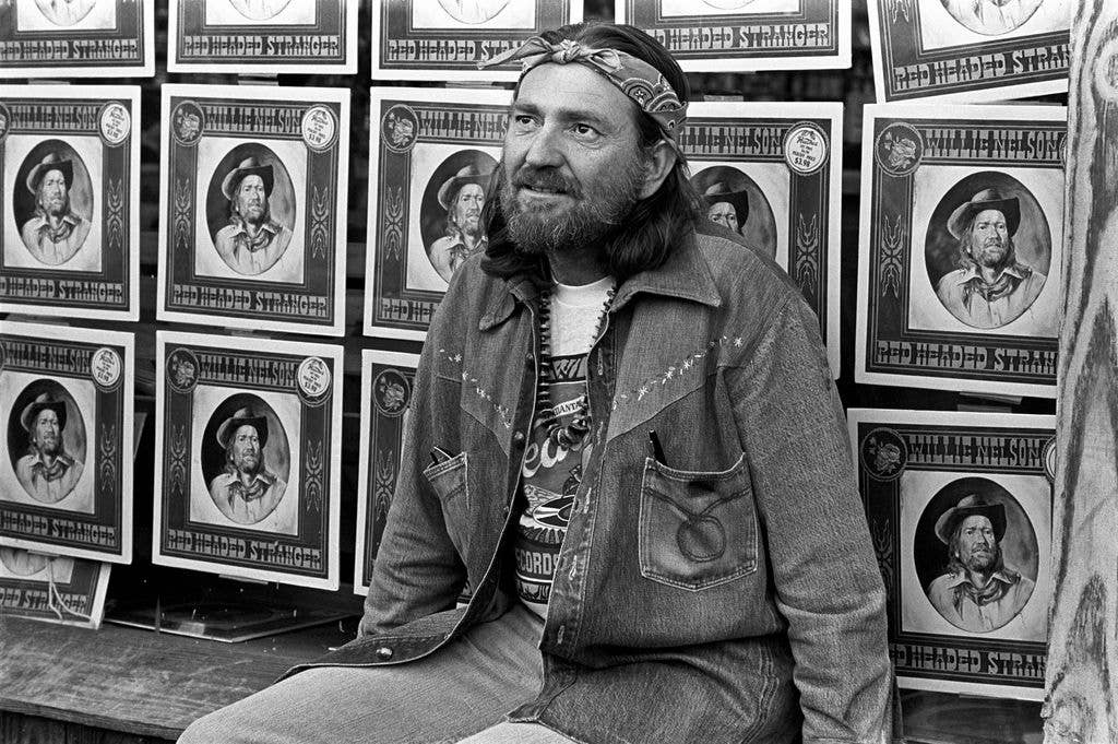 Willie Nelson sits in front of several poster print outs to promote his 'Red Headed Stranger' album in 1975.