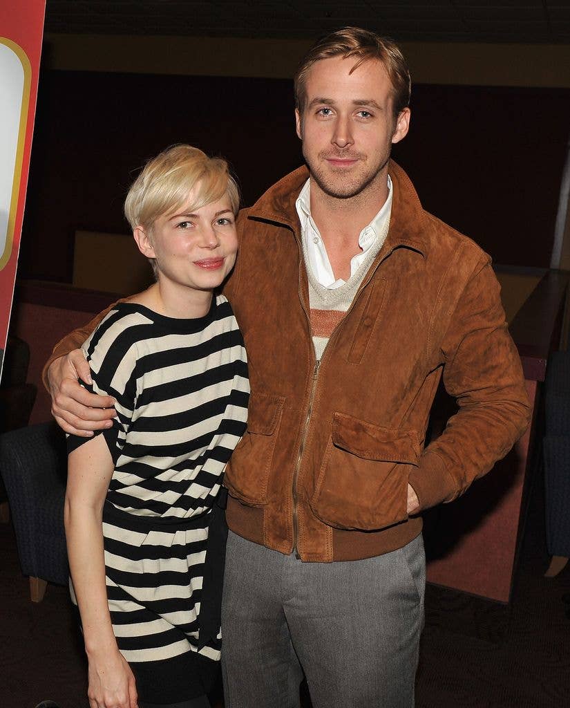 Michelle Williams wears a striped boatneck top and stands next to Ryan Gosling who wears a white shirt, brown suede jacket and jeans with his arm around her shoulders.
