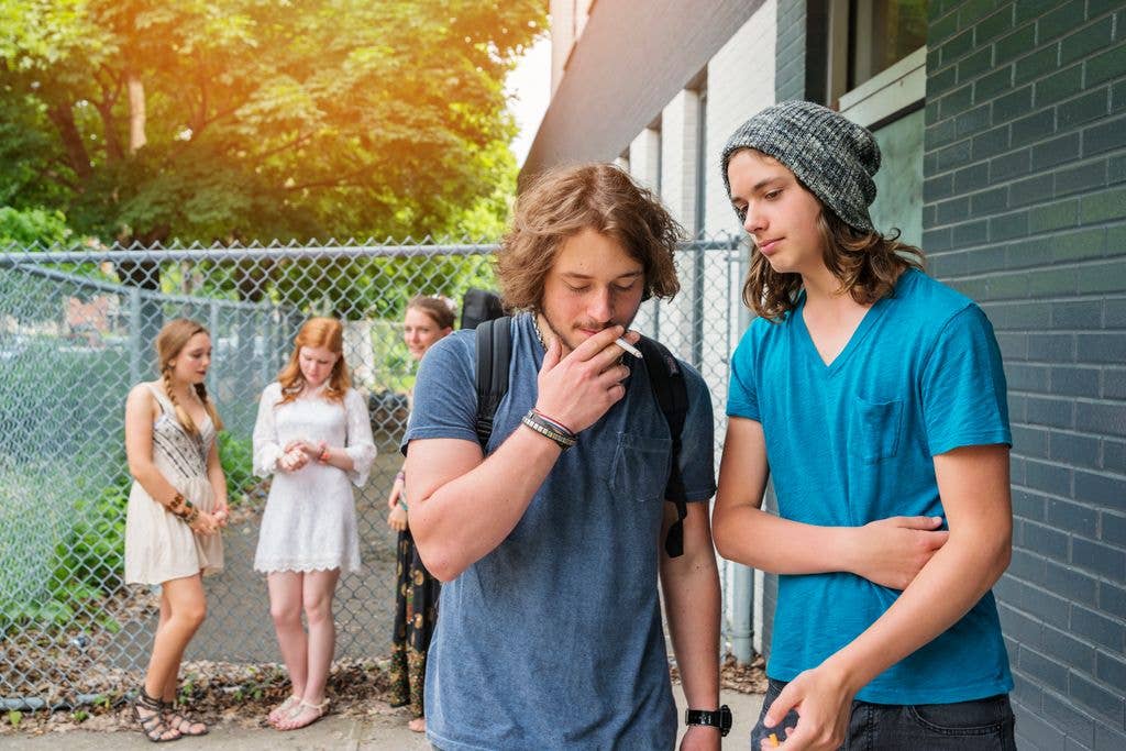 Two adolescent males smoking as three girls look on