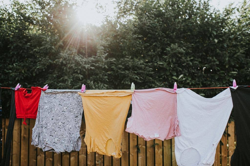 Various colours and sizes of clothing hanging in a row on a washing line outside, attached to the line with plastic clothes pegs