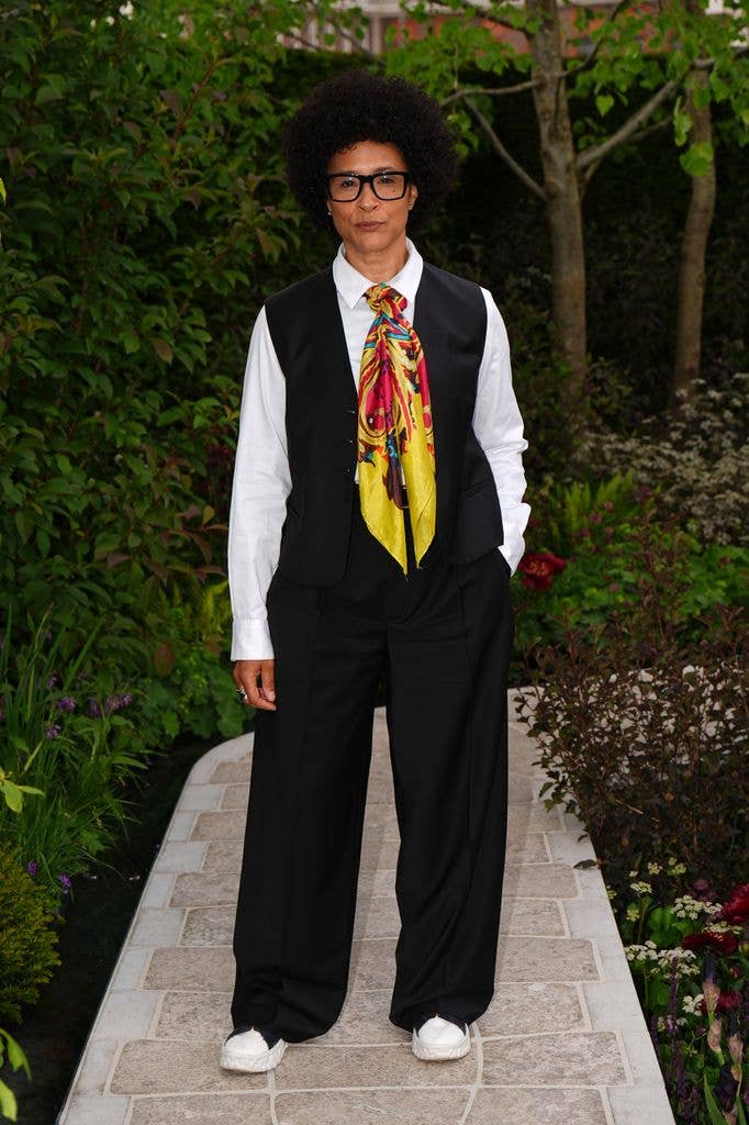 Golda Rosheuvel wears a black waistcoat, white shirt, black trousers and a yellow silk scarf tied around her neck. 