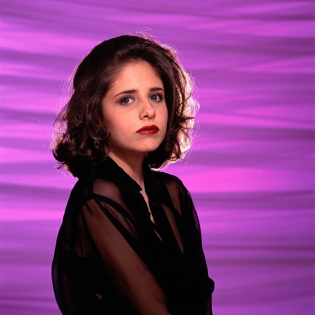 Sarah Michelle Gellar with a brown full bob, wearing a sheer black shirt and facing her body to the right of the image while turning her head to stare at the camera.