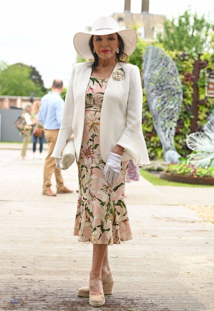 joan collins posed in floral dress and white hat