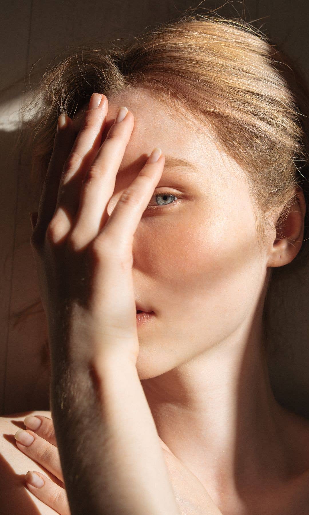 Model holding her hand up to cover half her face with her hand to reveal one eye 