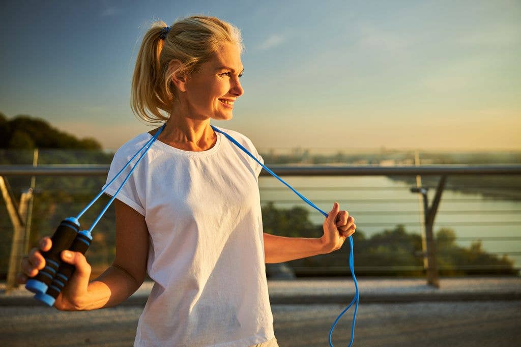 A woman in a white t-shirt is smiling while holding blue resistance bands.