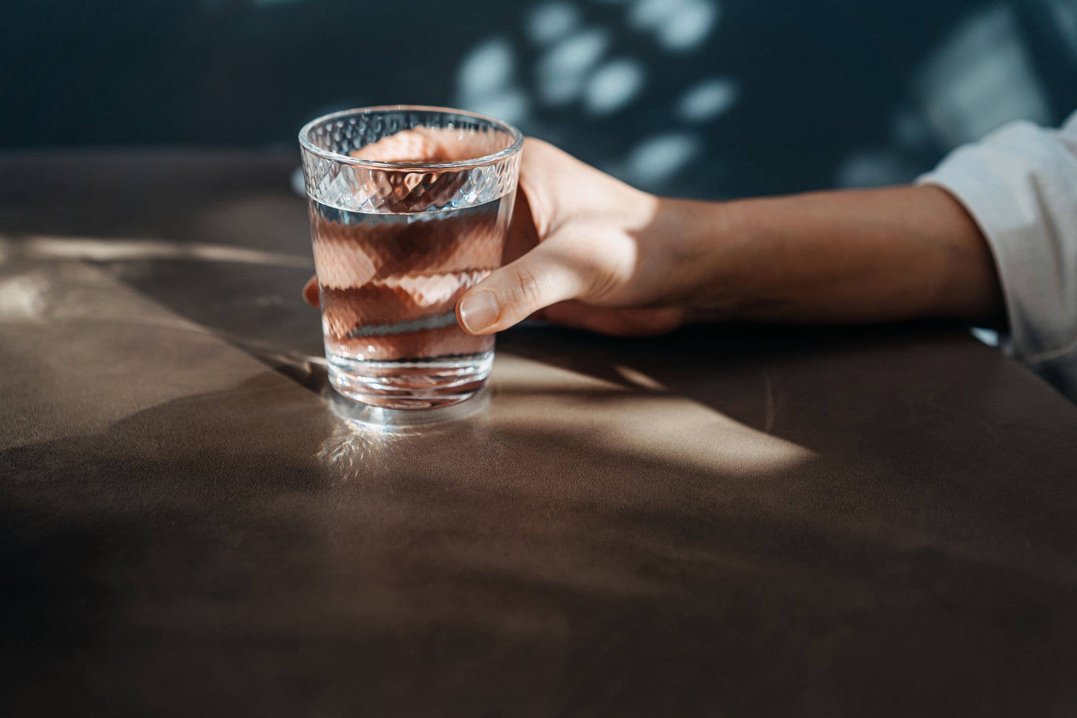 Close-up shot of a young Asian woman drinking a glass of water while sitting in dining table in restaurant. Female hand holding a glass of water. Healthy lifestyle. Staying hydrated