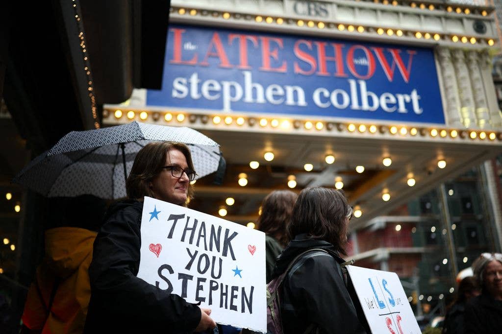 People hold signs supporting Stephen Colbert outside the Ed Sullivan Theater ahead of the taping of the final episode