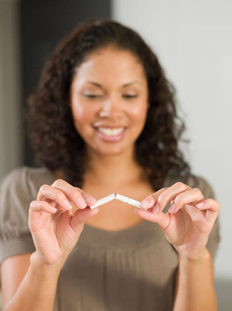 A woman with curly hair holds two broken cigarettes, smiling.