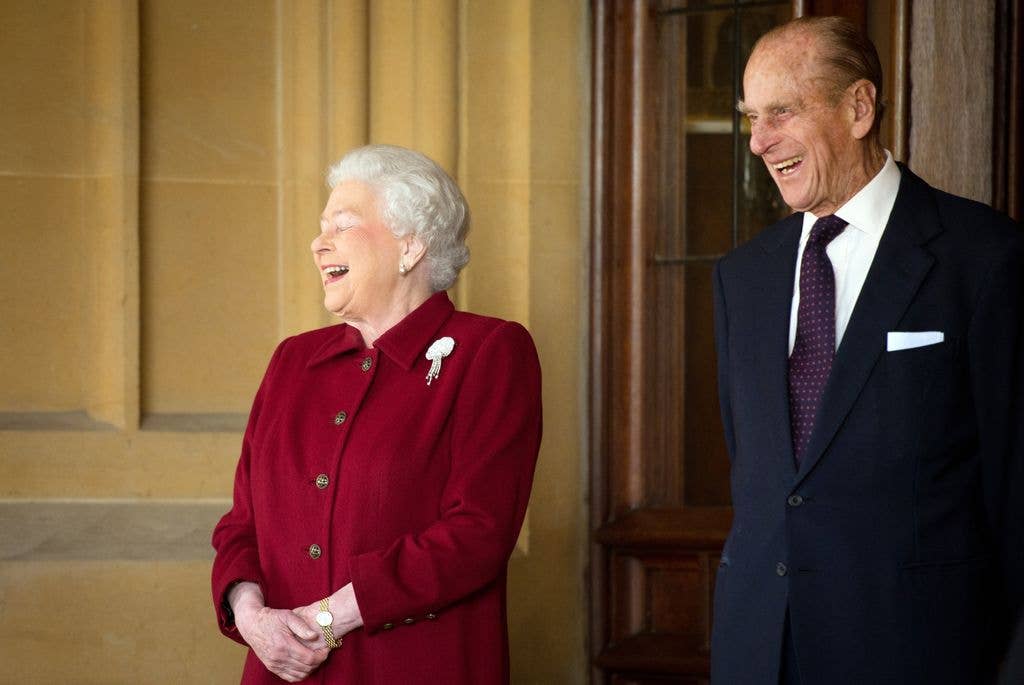 Queen Elizabeth II laughing whilst wearing a red coat and Prince Philip smiling in a blue suit